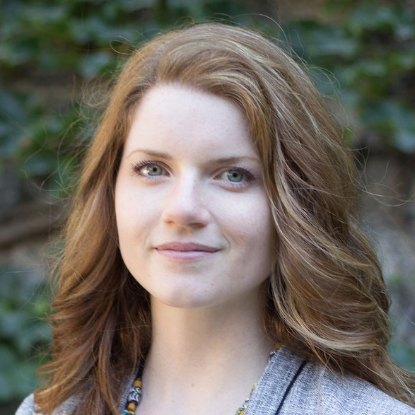 Woman with long brown highlighted hair wearing a gray suit jacket.