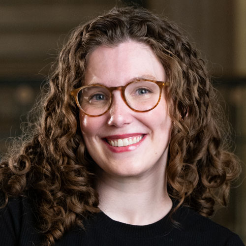 A woman with wavy auburn hair and tortoise rimmed glasses wearing a black blouse.