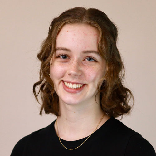 Woman with wavy auburn shoulder length hair in a black shirt.