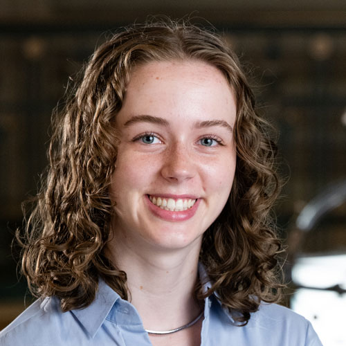 Woman with wavy auburn shoulder length hair in a light blue shirt.